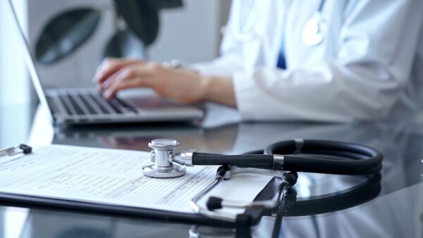 Stethoscope and medication record form are on the table besides the working doctor. Workplace in Medicine and Health care