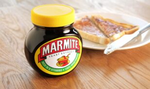 Jar of Marmite, unopened. Slice of toast on a white plate in background. Marmite is a food paste, made from yeast extract and has a distinctive salty flavor.