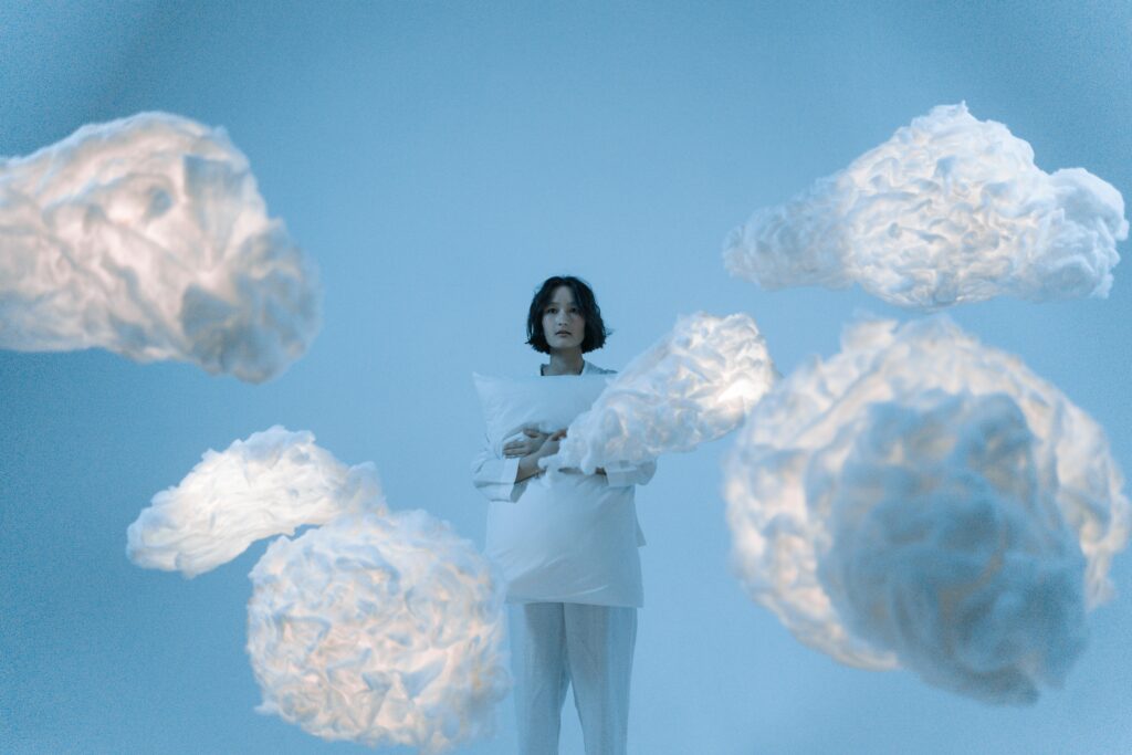 Woman on Heaven Background with a handmade clouds and a pillow in her hands