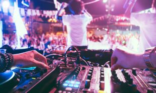 Dj mixing outdoor at beach party festival outdoor with crowd of people in background - Soft focus on left hand - Fun, summer, youth, nightlife, music, nightclubs and entertainment concept