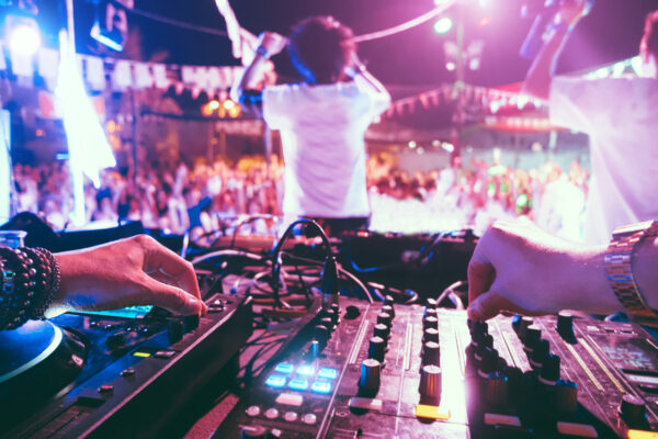 Dj mixing outdoor at beach party festival outdoor with crowd of people in background - Soft focus on left hand - Fun, summer, youth, nightlife, music, nightclubs and entertainment concept