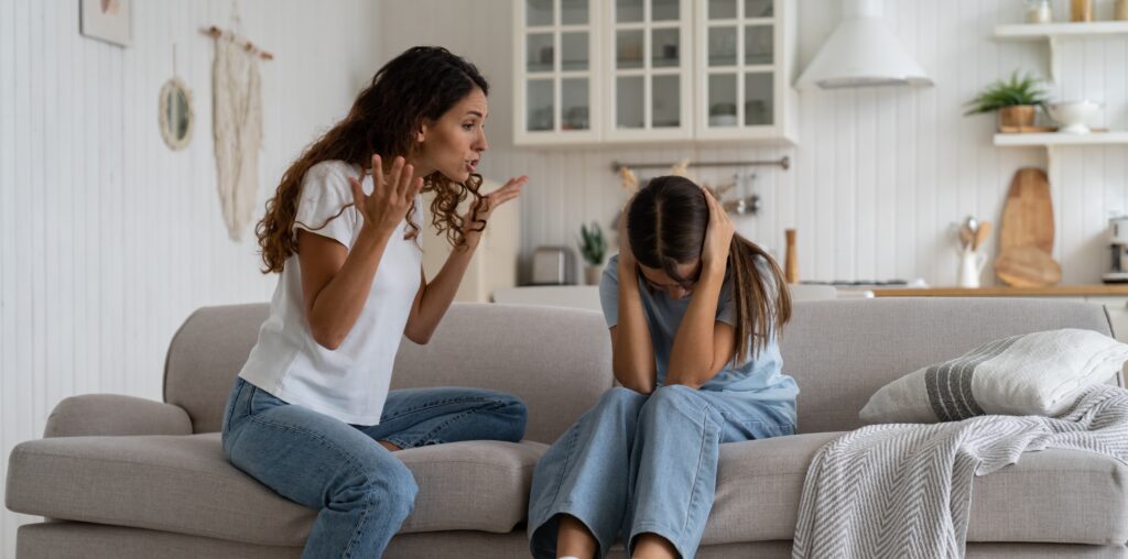 Angry mad mother trying to discipline child, expressing frustration shouting at teenage daughter sitting on sofa covering ears with hands. Psychological effects of yelling at kids, verbal abuse
