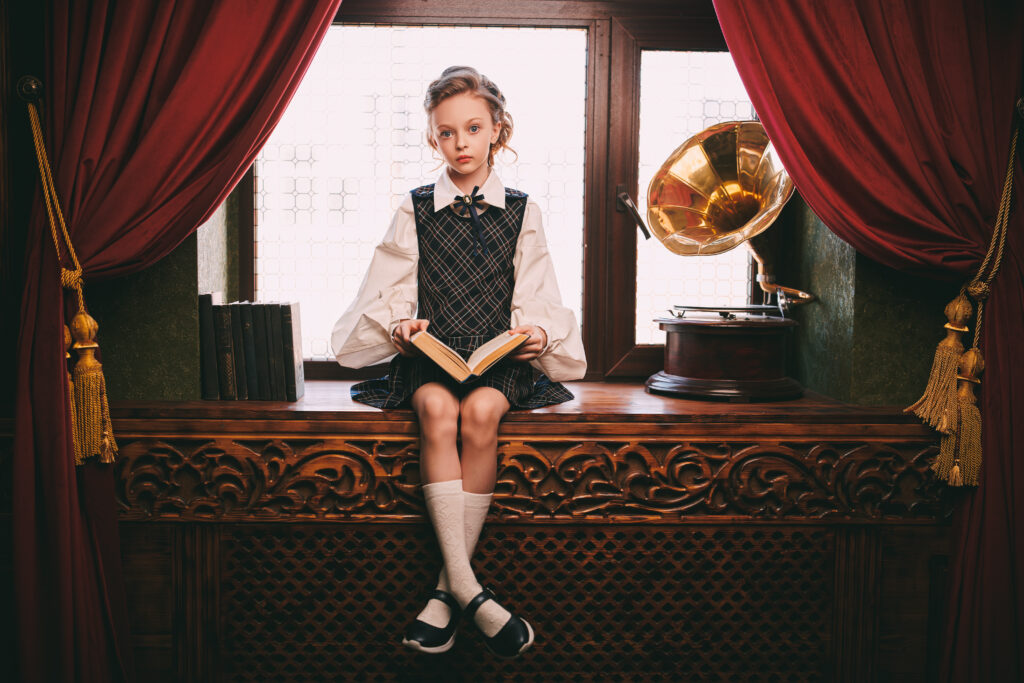 Cute eight year old girl in elegant classic school uniform sits in a luxurious vintage room and reads a book. Kid's school fashion.