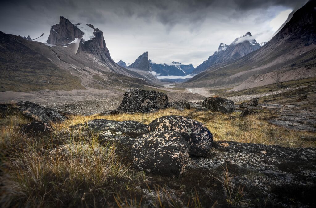 Wild Weasel river winds through remote arctic valley of Akshayuk Pass, Baffin Island, Canada on a cloudy day. Dramatic arctic landscape with Mt. Breidablik and Mt. Thor. Autumn colors in the arctic