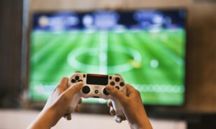 Person Holding Game Pad in front of a screen with a football game on it