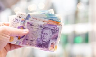 Close-up of a hand holding British pound banknotes (£5, £10, £20), featuring King Charles III. Useful for finance, banking, currency exchange, and economic themes.