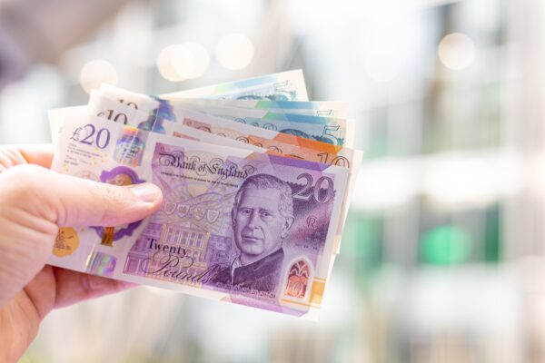 Close-up of a hand holding British pound banknotes (£5, £10, £20), featuring King Charles III. Useful for finance, banking, currency exchange, and economic themes.