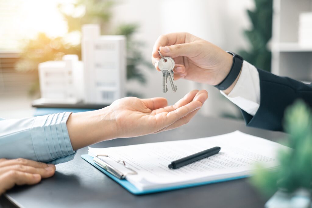 Real estate agent handed over the key to new home, marking a successful investment in business of property, whether it be a house or an apartment. Real estate agent giving house key to customers.