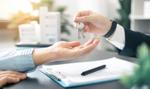 Real estate agent handed over the key to new home, marking a successful investment in business of property, whether it be a house or an apartment. Real estate agent giving house key to customers.
