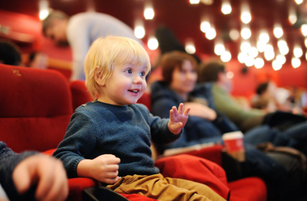 Cute toddler boy watching cartoon movie in the cinema. Leisure/entertainment for family with kids.