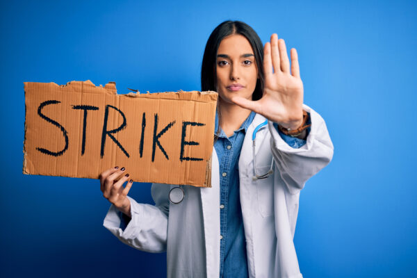 Young doctor woman wearing stethoscope holding cardboard banner protesting in strike with open hand doing stop sign with serious and confident expression, defense gesture