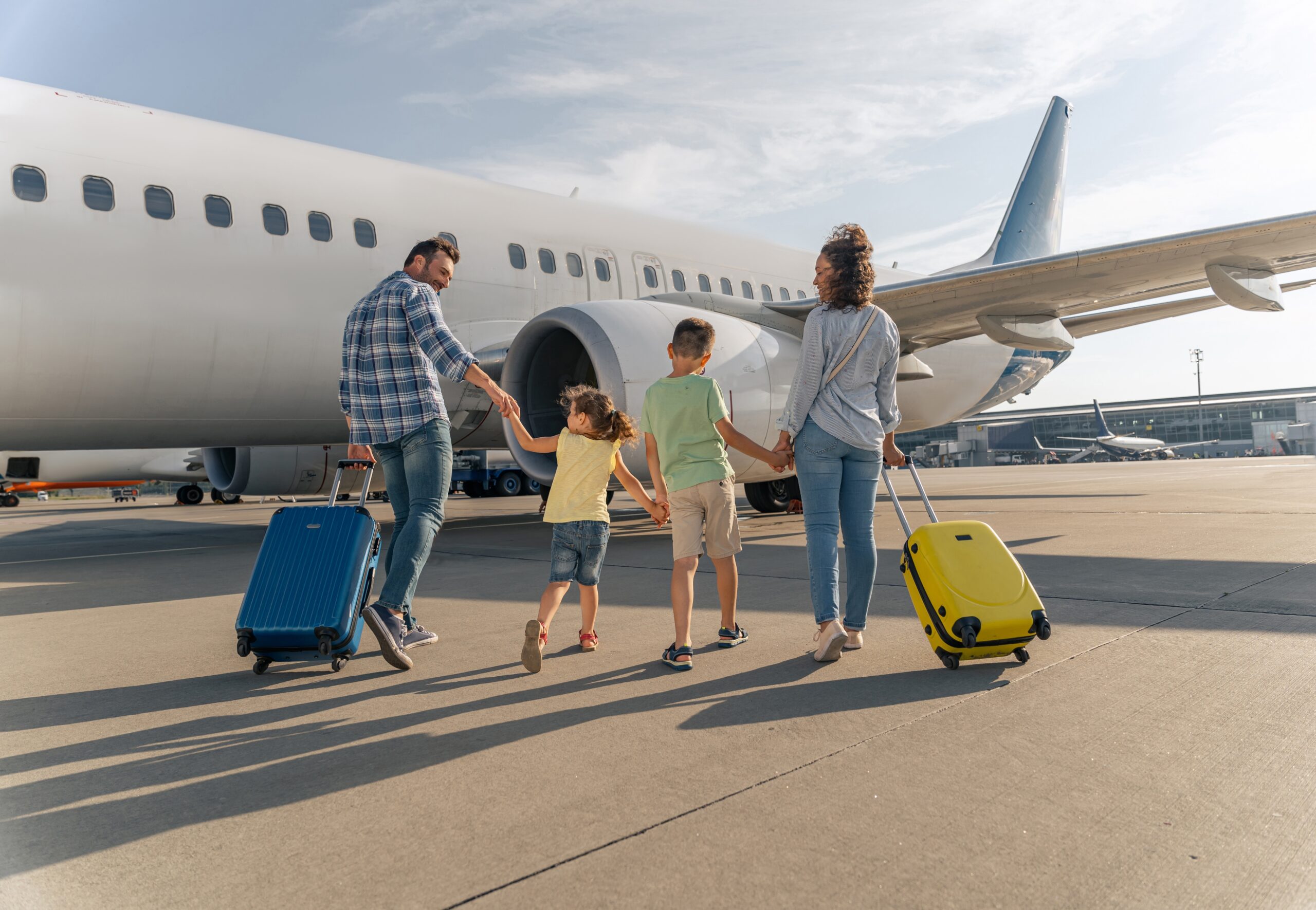 Smiling parents and kids walking with travel bags with a big plane in the background. Trip concept