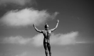 Grayscale photo of back side of statue of man raising his arms