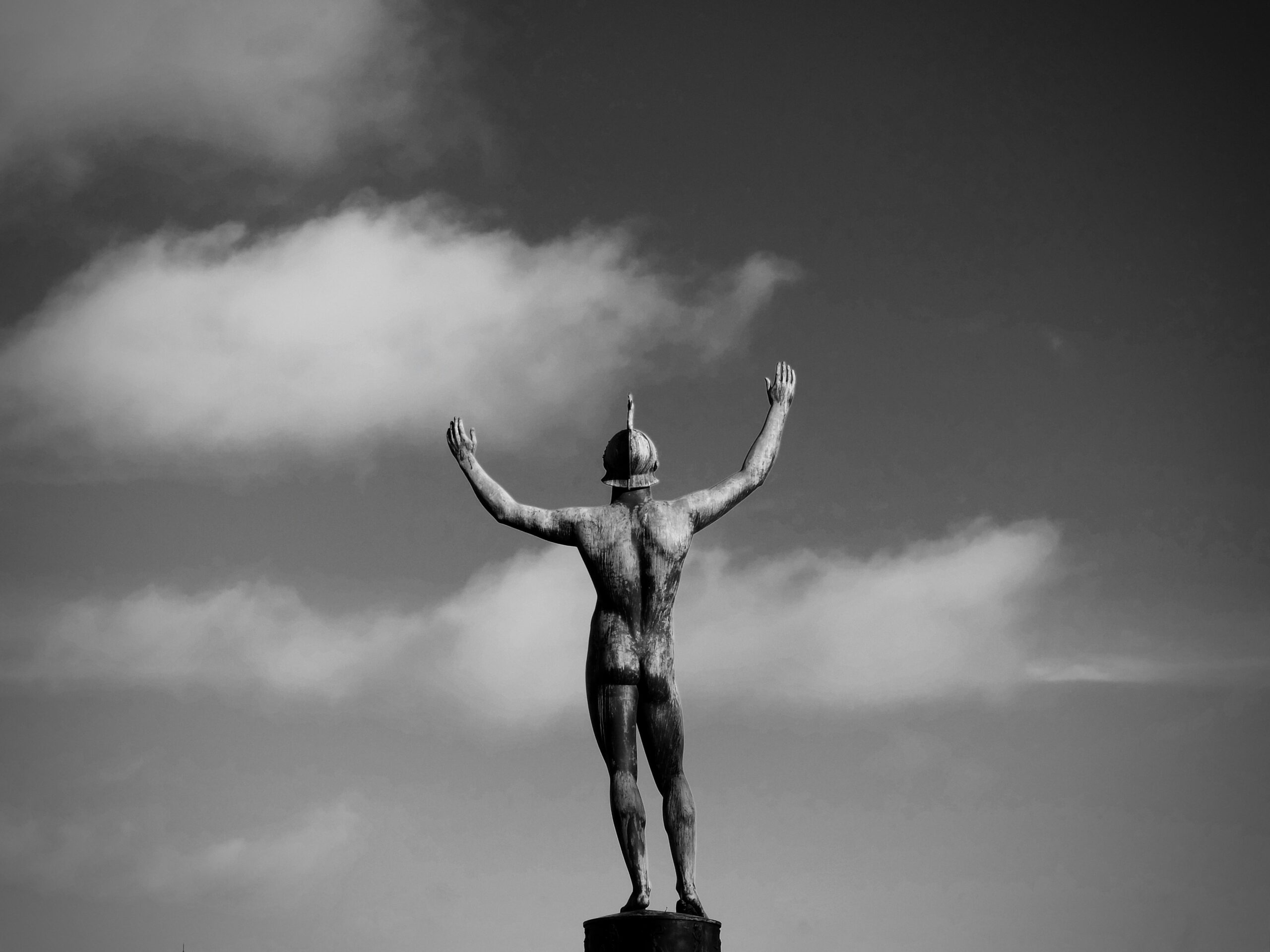 Grayscale photo of back side of statue of man raising his arms