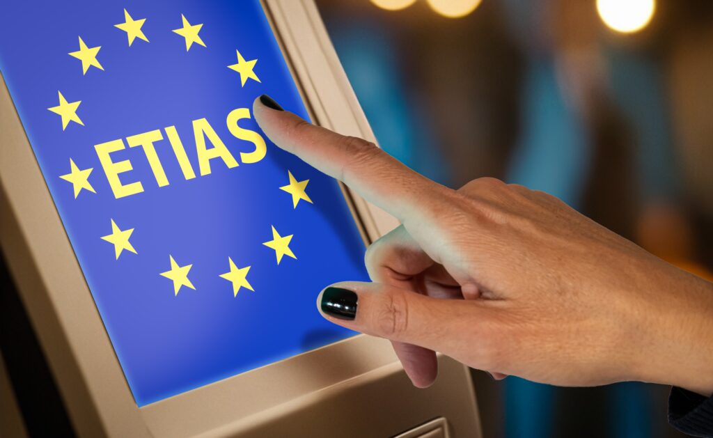 Close-up of a hand pointing at a touchscreen displaying the ETIAS logo with EU stars, symbolizing the European Travel Information and Authorization System process