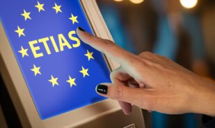 Close-up of a hand pointing at a touchscreen displaying the ETIAS logo with EU stars, symbolizing the European Travel Information and Authorization System process