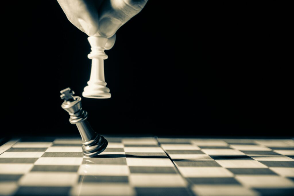 grayscale photo of a hand knocking a black king off the chess board with a white king