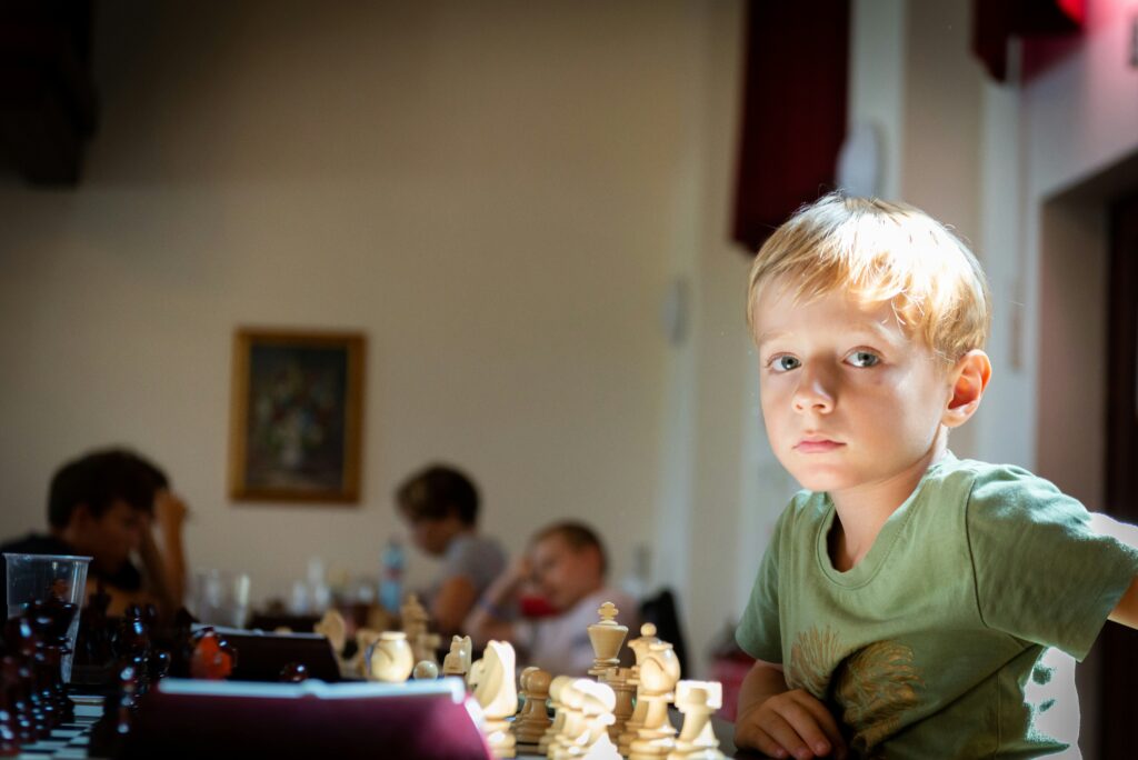 boy in green crew neck shirt sitting on chair by a chess board