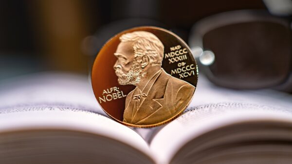 Alfred Nobel's image on gold coin on physics book and reading glasses in background. Nobel Prize award. Nobel Prize for Literature concept.