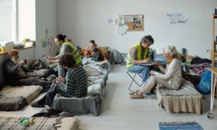 Two volunteers in uniform sitting in front of refugees and taking notes while asking personal questions to homeless people
