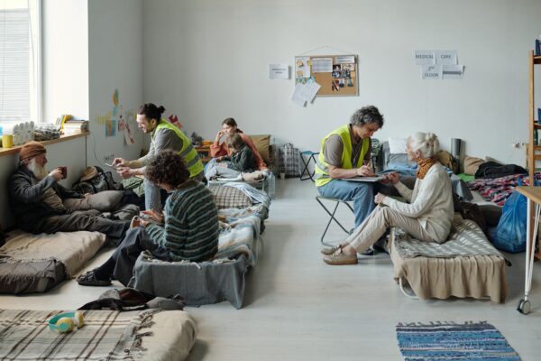 Two volunteers in uniform sitting in front of refugees and taking notes while asking personal questions to homeless people