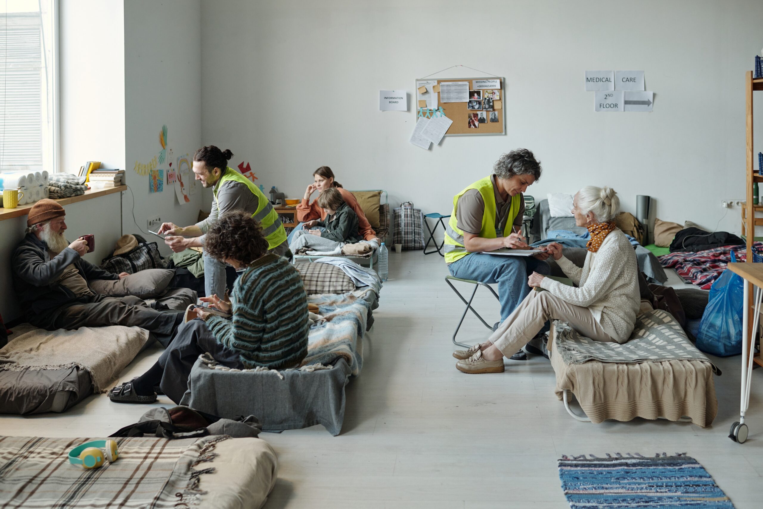 Two volunteers in uniform sitting in front of refugees and taking notes while asking personal questions to homeless people