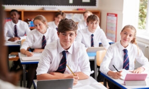 Students from private school wearing uniform Listening To Female Teacher In Classroom
