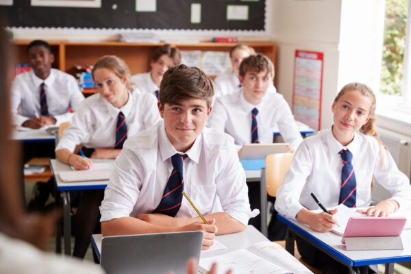 Students from private school wearing uniform Listening To Female Teacher In Classroom