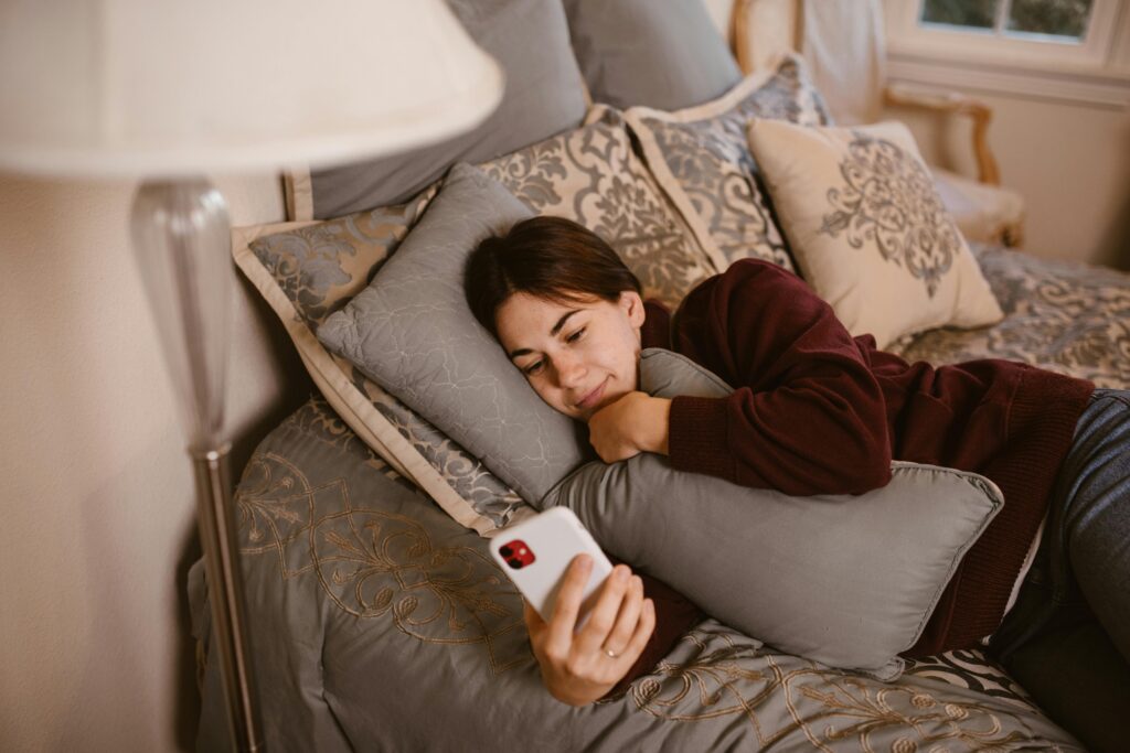 Woman Lying on Bed while Using Smartphone