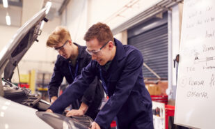 Two Male Students Studying For Auto Mechanic Apprenticeship At College Working On Car Engine