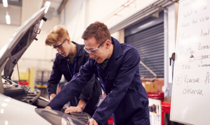 Two Male Students Studying For Auto Mechanic Apprenticeship At College Working On Car Engine