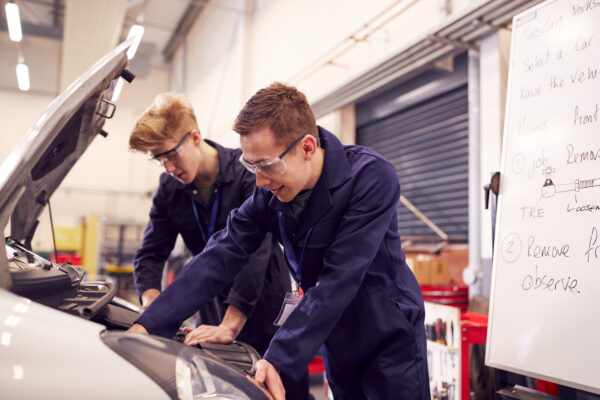 Two Male Students Studying For Auto Mechanic Apprenticeship At College Working On Car Engine