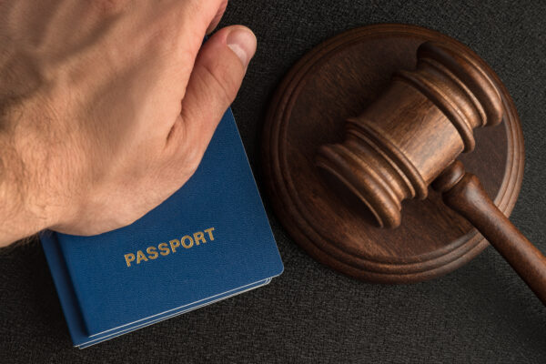 Male hand holds passport next to wooden gavel. Obtain citizenship. Legal immigration