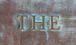 THE: Lettering THE on a bronze plate. Close-up of definite article THE on a bronze slab with oxidized green patina. Inscription on a bronze monument