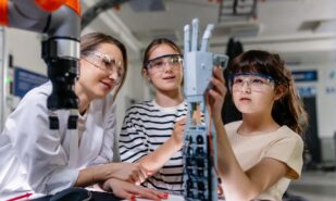 Mom and daughters during take your kid to work day, encouraging them in career in robotics. Field trip to real robotics laboratory. Real scientist talking to girls, showing prosthetic robot hand.