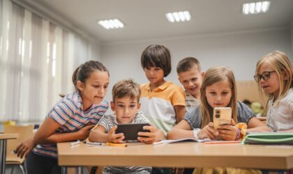 Young students use cellphone for video games on a break in the classroom at school