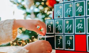 Child opens Christmas advent calendar doors on christmas tree background.Gifts and surprises.Christmas Tree Advent Calendar and a child in a bright, cozy room