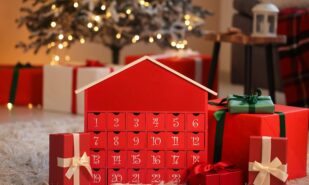 Red advent calendar with gift boxes on floor near Christmas tree at home