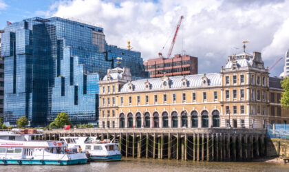 Old Billingsgate fish market next to a modern glass building on the banks of the River Thames in the city of London