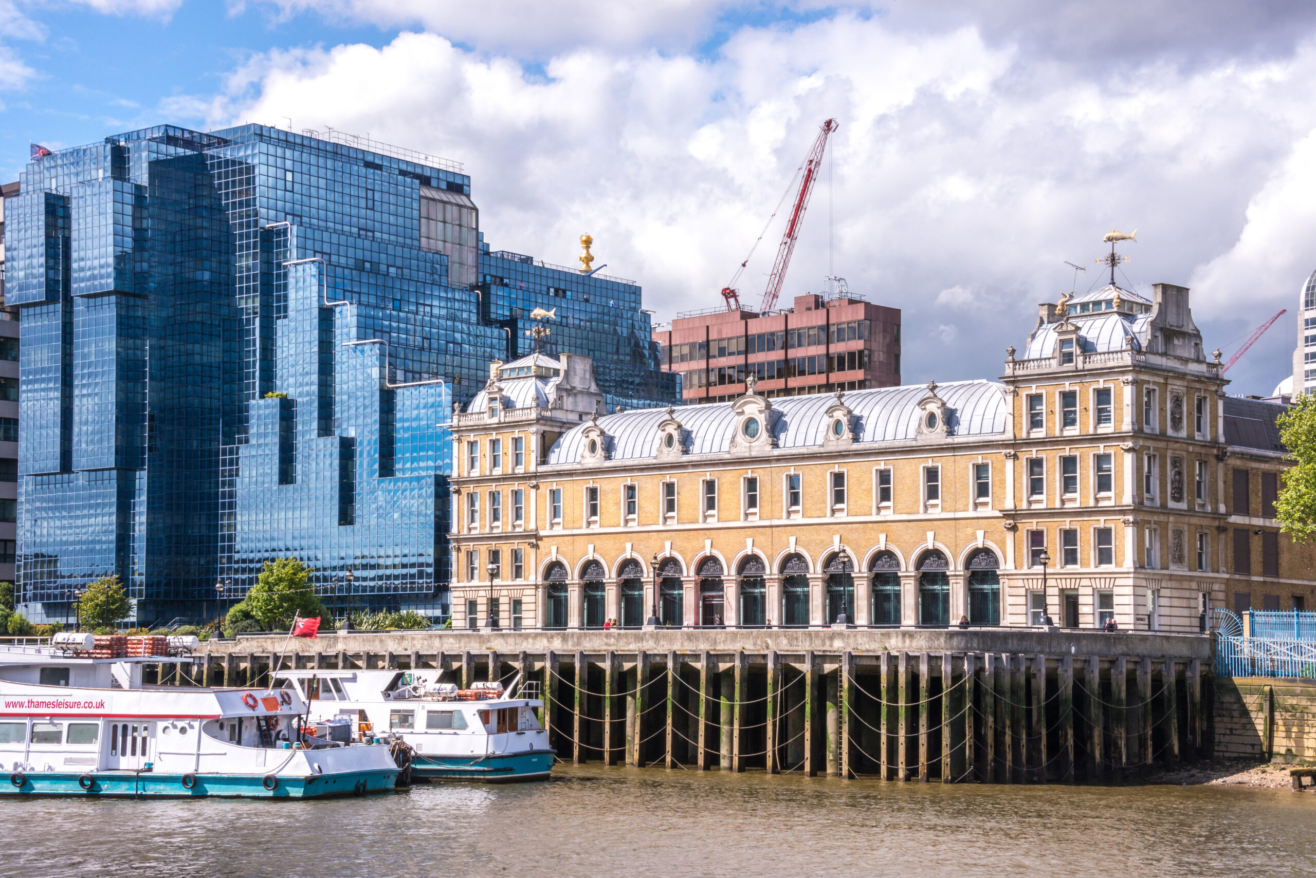 Old Billingsgate fish market next to a modern glass building on the banks of the River Thames in the city of London