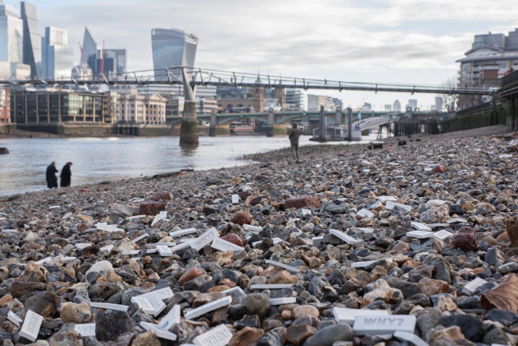 Tiles with the questions 'WHEN?' and 'WHY?' by artist 742 among pebbles on the Thames in London, UK