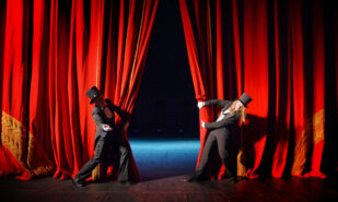 Actor and actress in tuxedos open theater curtain