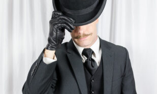 Portrait of British Gentleman in Dark Suit and Leather Gloves Politely Doffing Bowler Hat. Suave Spy Hero with Jaunty Moustache.