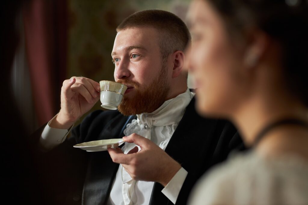 Side view portrait of young gentleman sipping tea delicately from porcelain teacup in classic setting