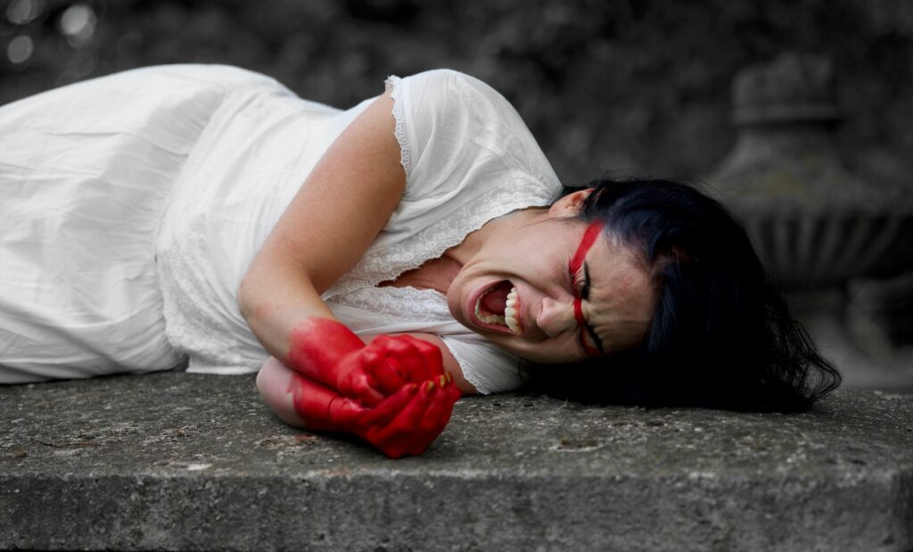 woman in white dress with hands covered in red paint yelling on the ground