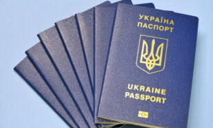 Ukraine passports with golden trident emblem and letters on blue blurred background. Stack of id ukranian documents with selective focus.