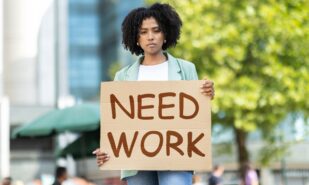 Unemployed pretty young black woman wearing casual outfit standing on street, holding Need Work placard, upset unhappy african american lady attending unemployment strike