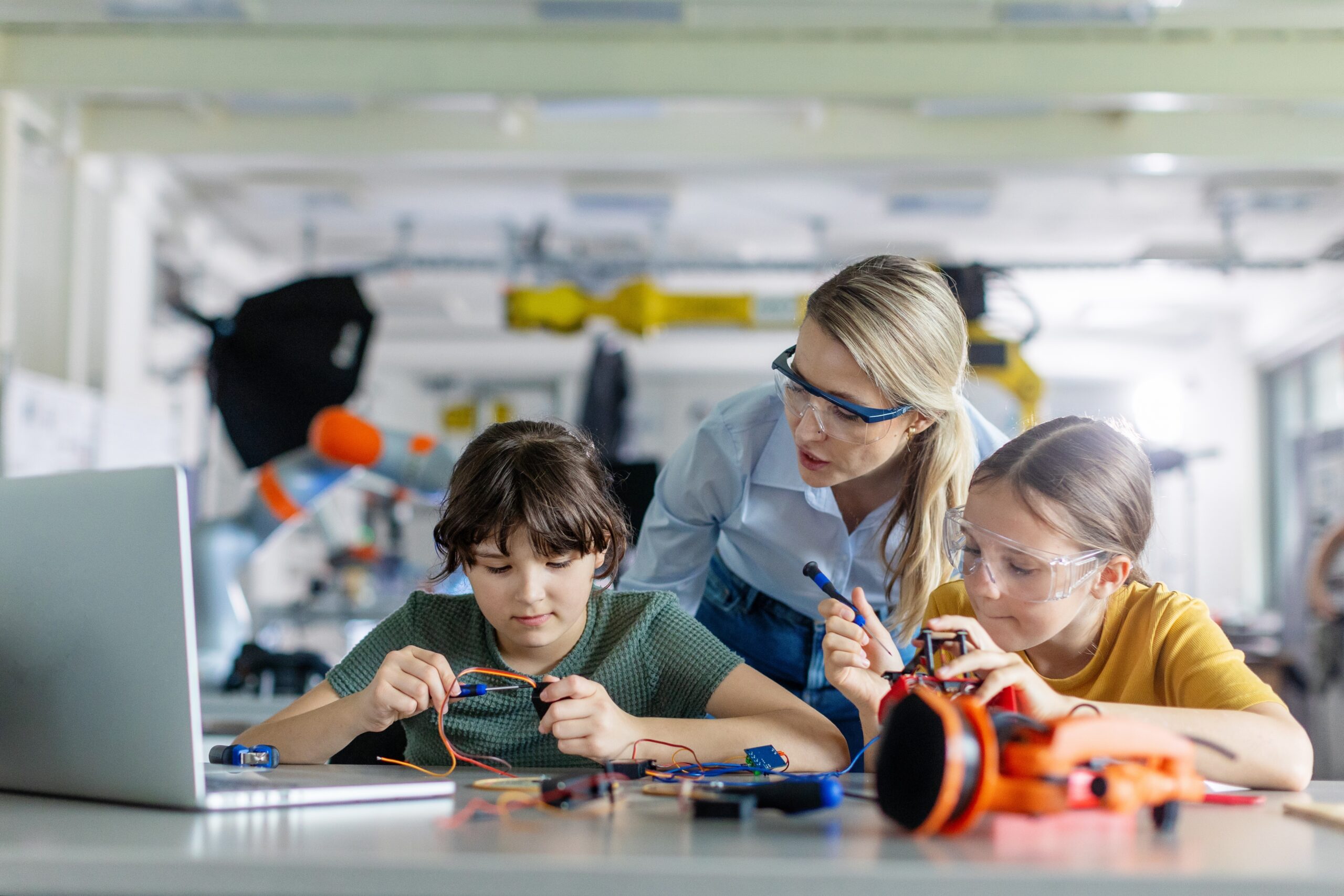 Female teacher helping to girls working on small robot, building robotic car in after-school robotics club. Children learning robotics in Elementary school. Girls in science.